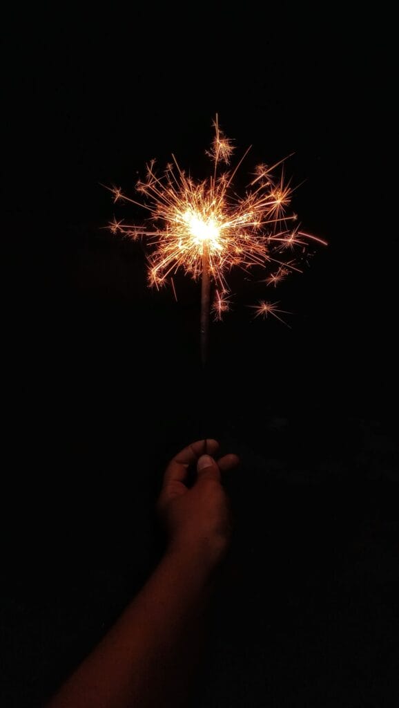 A captivating image of a hand holding a bright sparkler against a dark background, illuminated with vibrant sparks.