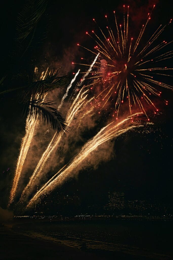 Spectacular fireworks illuminate the night sky in Honolulu, Hawaii, with palm trees in silhouette.